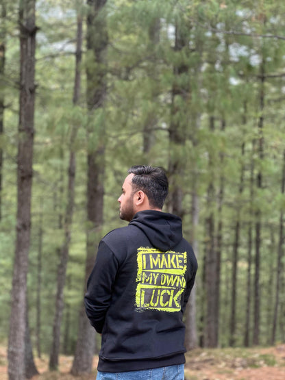 Black graphic hoodie with 'I MAKE MY OWN LUCK' text design on the back, worn in a forest setting. Stylish and comfortable premium hoodie.