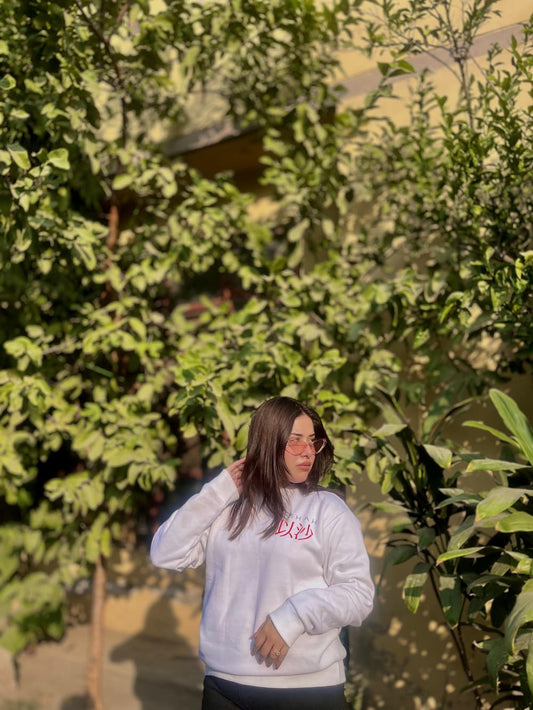 White custom-designed sweatshirt with red Arabic text, worn by a person outdoors. Stylish and cozy apparel, perfect for personalized fashion in Pakistan.