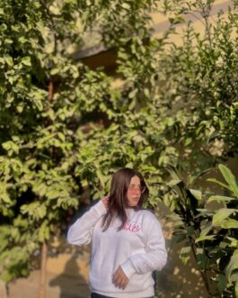 White custom-designed sweatshirt with red Arabic text, worn by a person outdoors. Stylish and cozy apparel, perfect for personalized fashion in Pakistan.